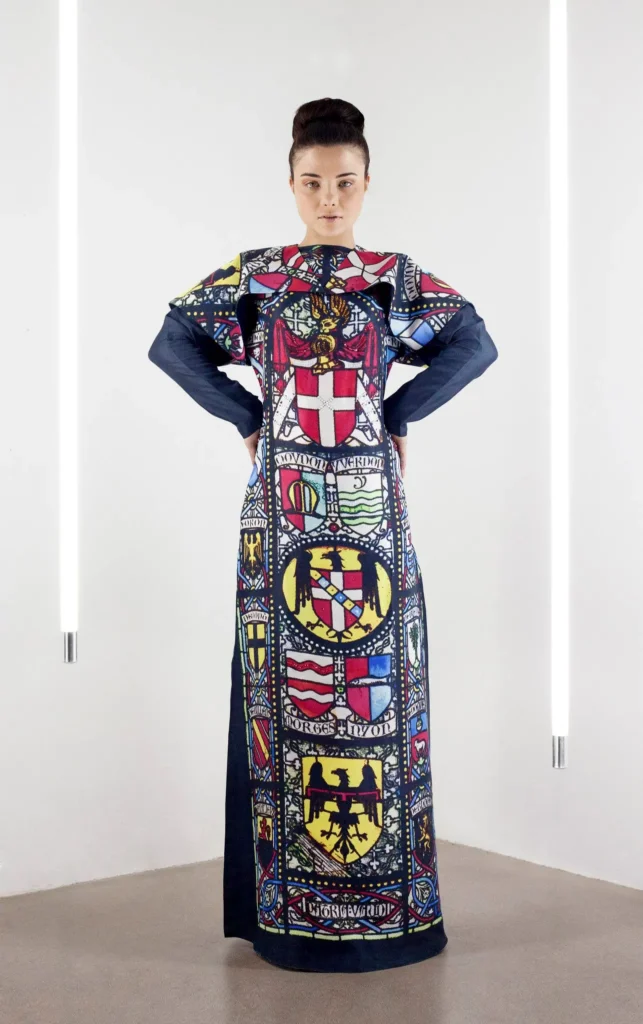 Model wearing a long-sleeve caped silk thobe-style dress with a print inspired by stained glass windows of European churches.